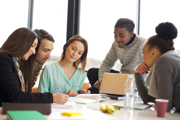 Group of five young adults sitting around a table working on something together