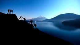 Hikers helping each other up a dark mountain